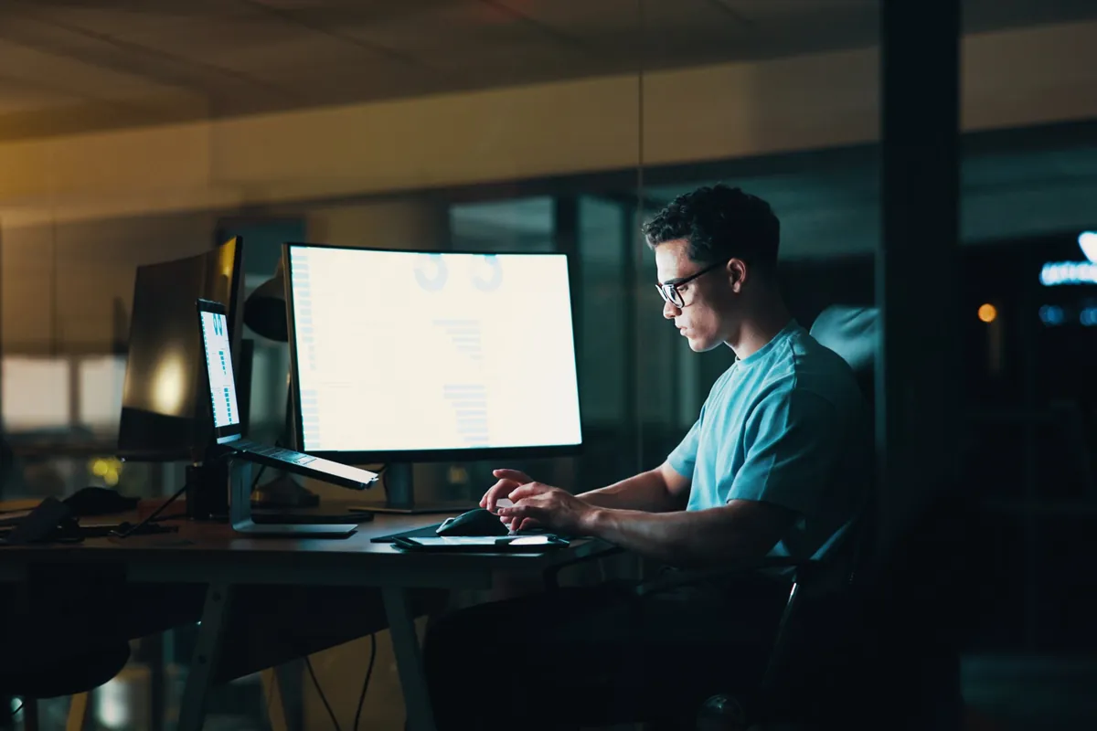 IT-Techniker arbeitet abends im Büro an mehreren Bildschirmen am Datenumzug in die Cloud