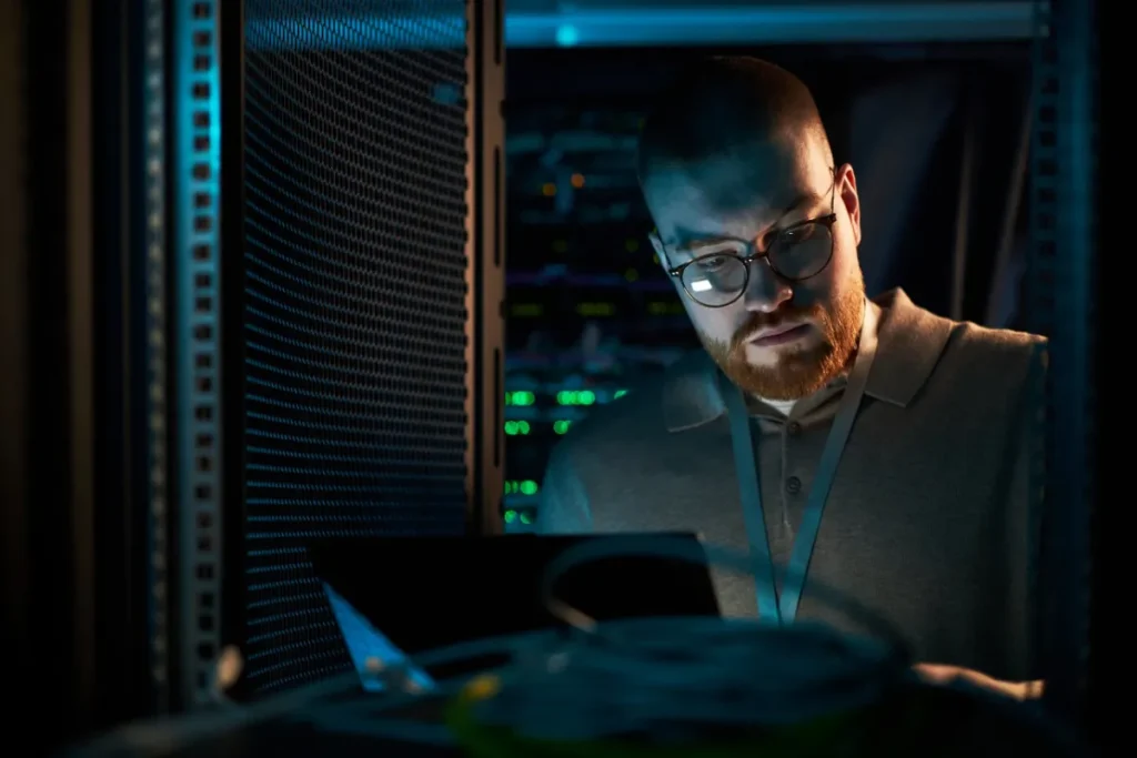 IT-Techniker prüft nachts im Serverraum am Laptop die Webserver auf die PHP-Sicherheitslücke PHP2Shell